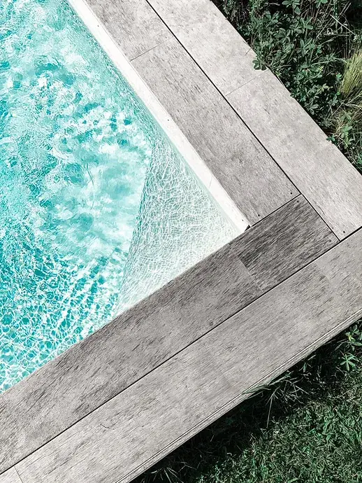 Esquina de una piscina con coronación de tablas de aspecto madera junto al agua