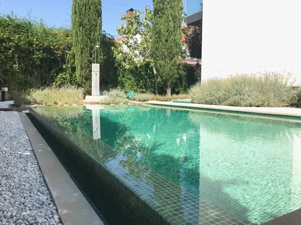 Piscina desbordante con borde de grava junto a una pared blanca
