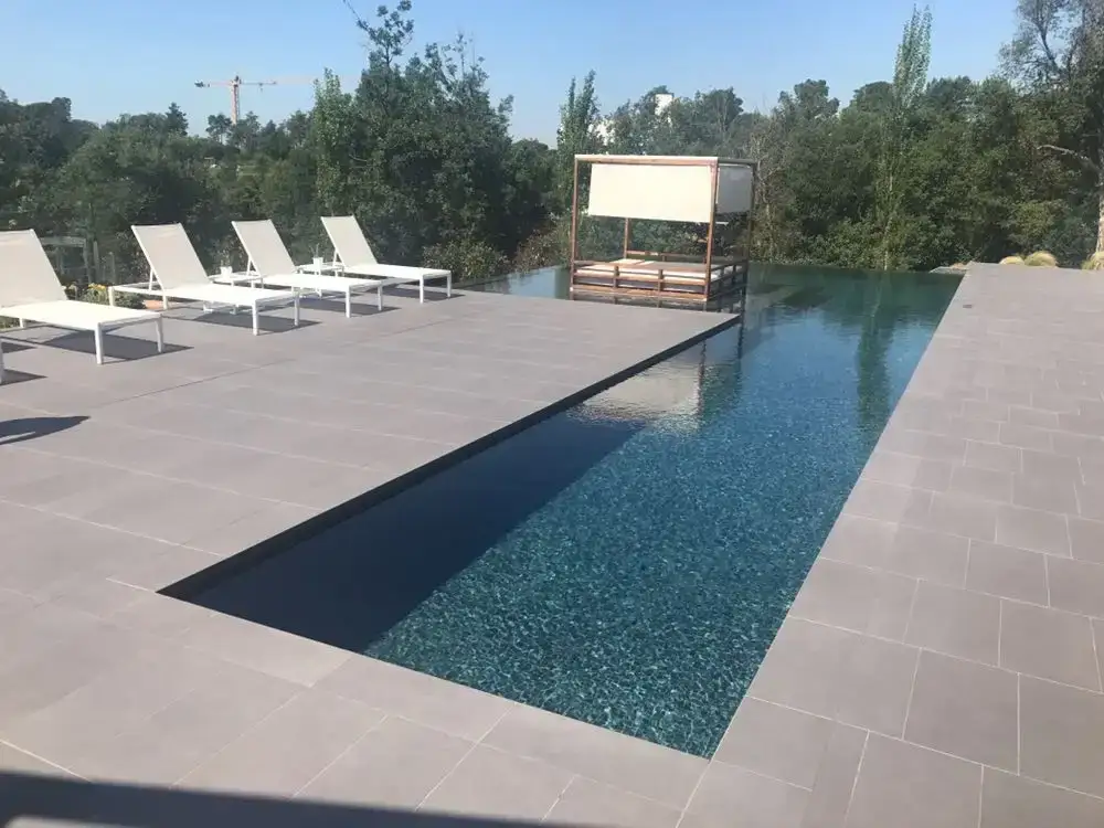Pavimento gris alrededor de una piscina con tumbonas blancas
