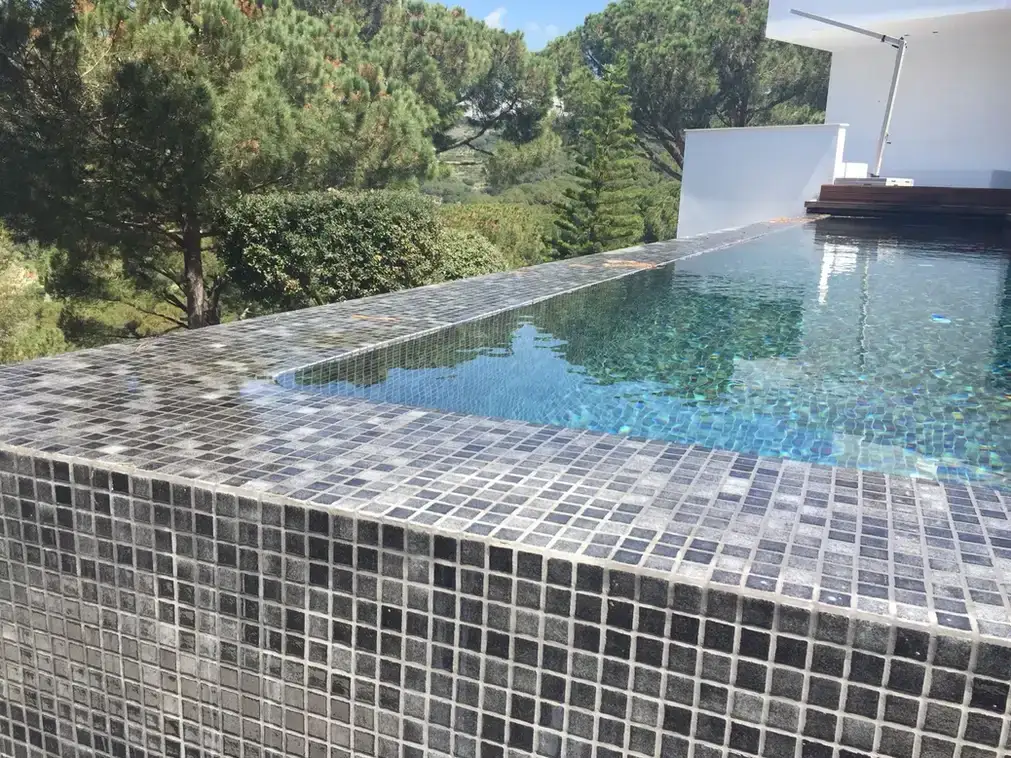 Piscina revestida de gresite gris en un jardín con árboles