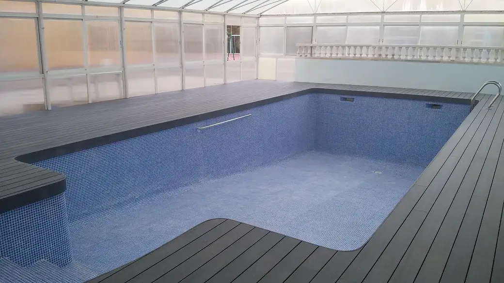 Piscina cubierta por un cerramiento de policarbonato, con tarima gris alrededor