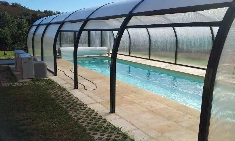 Cubierta curva de policarbonato sobre una piscina alargada, con los equipos al lado