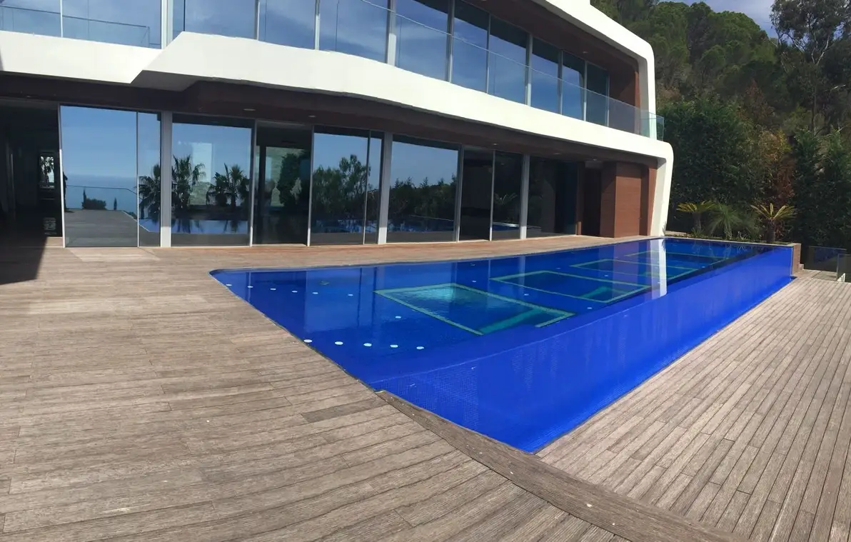 Piscina de gresite azul intenso rodeada de tarima de madera junto a una vivienda de líneas modernas