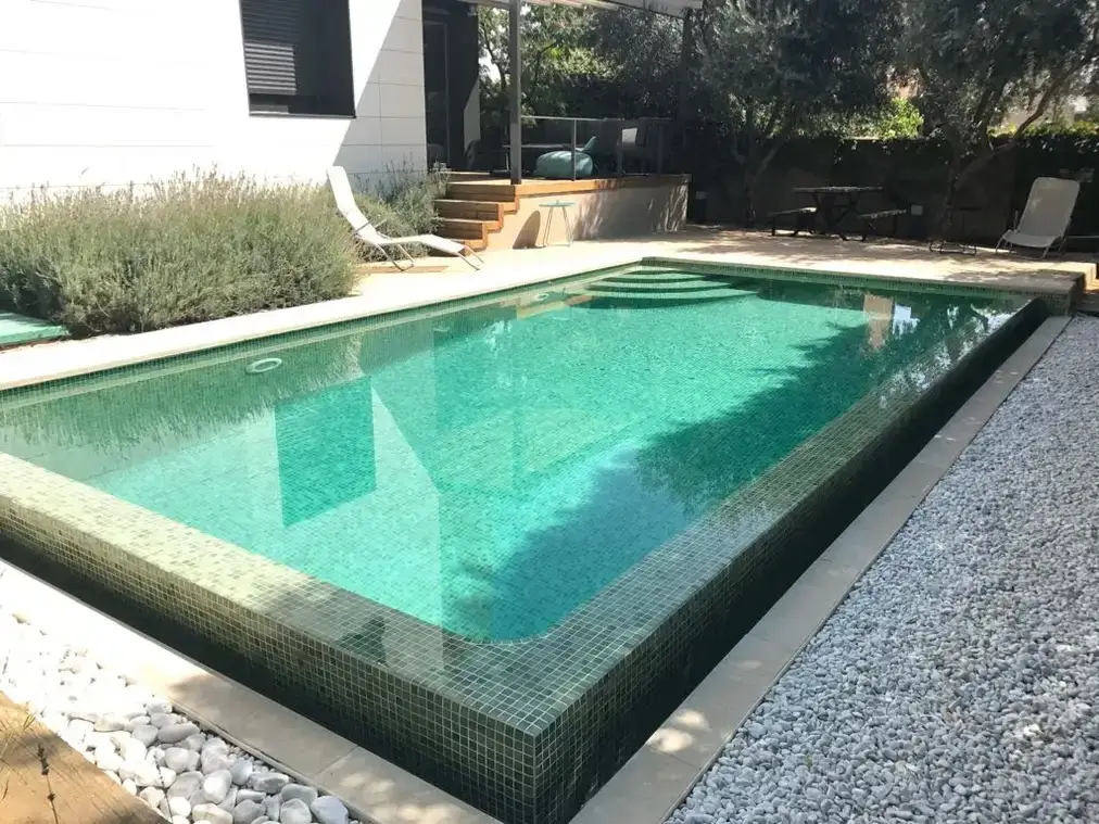 Piscina de gresite verde cuyo borde desborda sobre una franja de grava