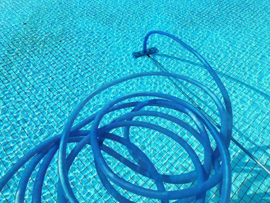 Manguera de limpiafondos enrollada en el fondo de una piscina