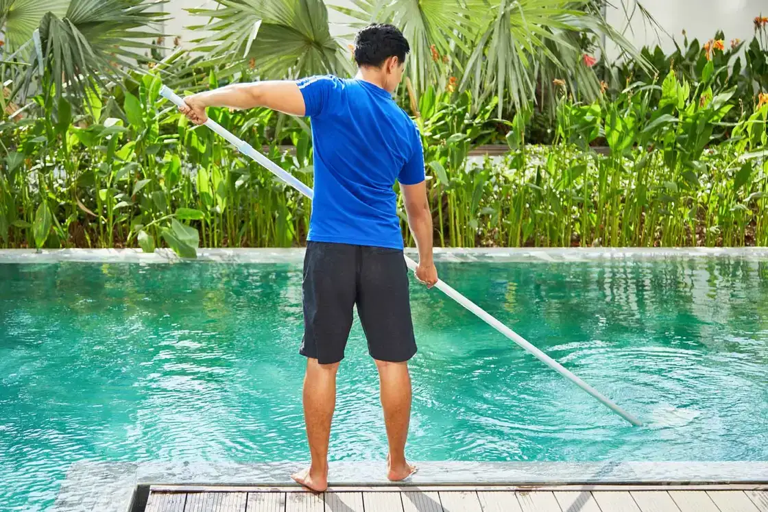 Operario limpiando una piscina con un recogehojas de mango largo
